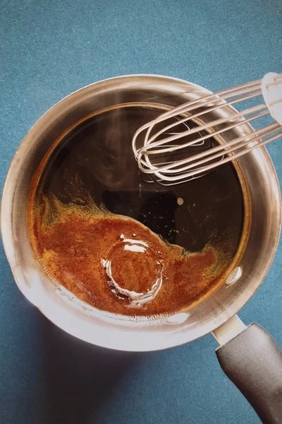 Top view of a saucepan with water, instant coffee powder and sugar in it with a whisk on the side