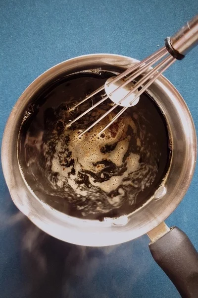 Top view of a saucepan with black coffee in it being stirred by a whisk