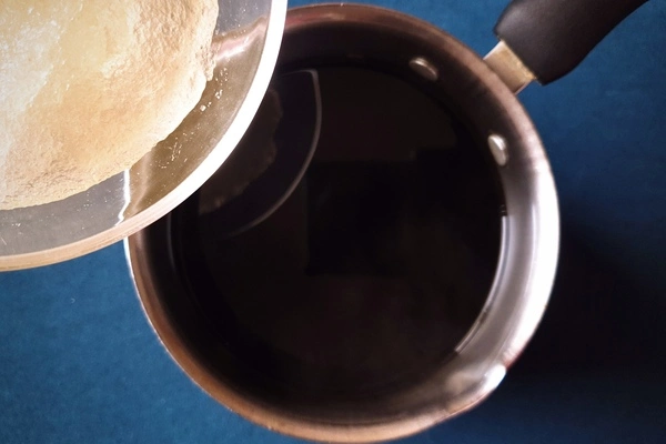 Top view of a saucepan with black coffee in it and a bowl of bloomed gelatin powder being poured from the side