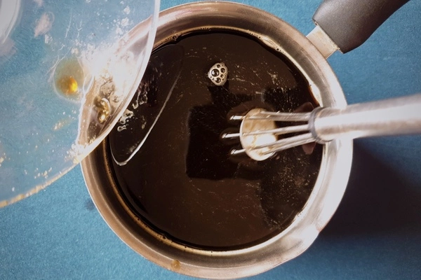Top view of a saucepan with black coffee and bloomed gelatin powder in it being stirred by a whisk