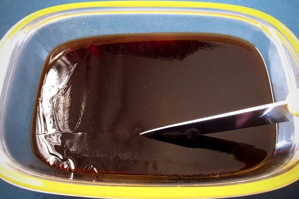 Coffee jelly in a glass tray being cut in horizontal lines with a knife