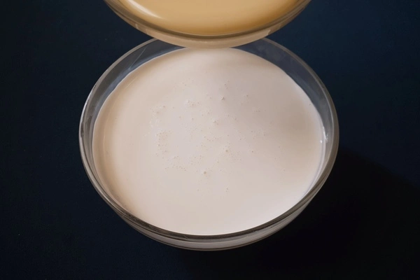A glass bowl filled with heavy cream in it and another glass bowl right above it filled with sweetened condensed milk