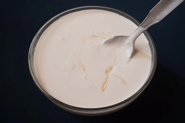 A glass bowl filled with heavy cream and sweetened condensed milk mixture being stirred with a spoon