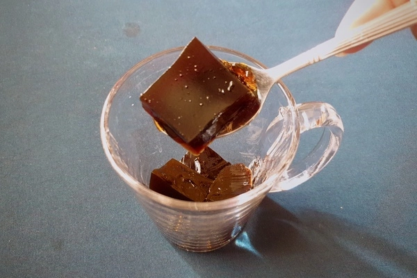 Cubes of coffee jello being poured into a glass mug with a spoon