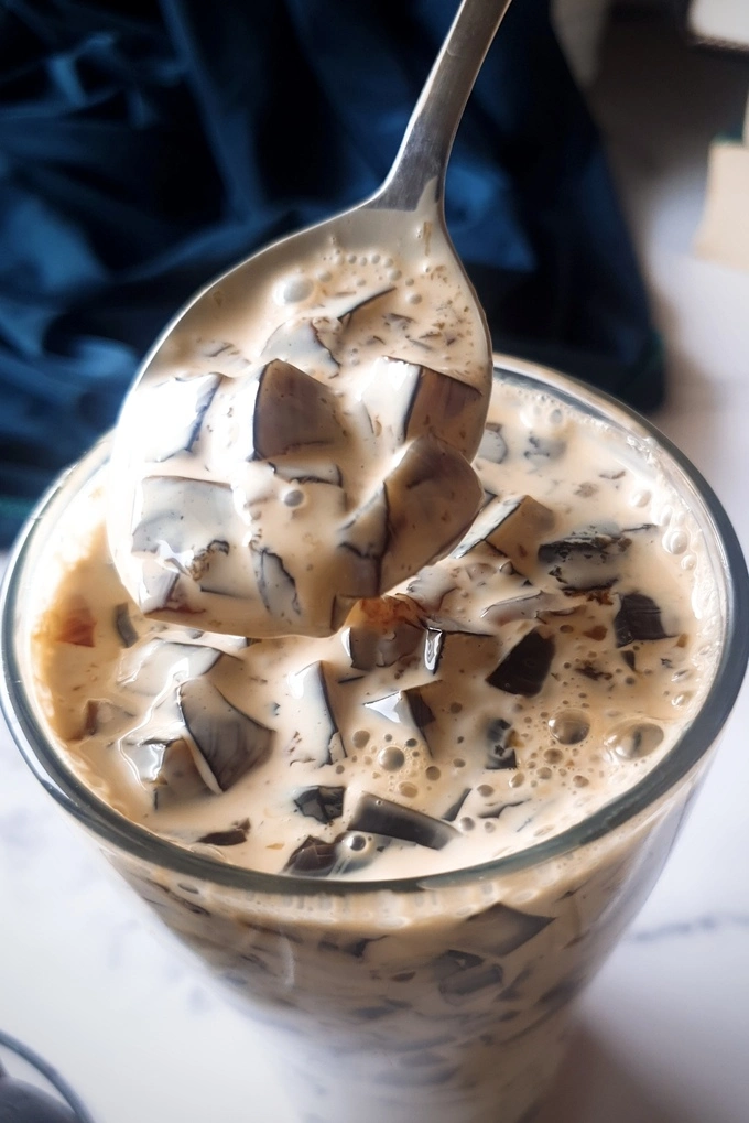 Close up of a glass filled with sliced Homemade Coffee Jello Recipe cut into small cubes with Condensed Milk Cream, being scooped up with a spoon