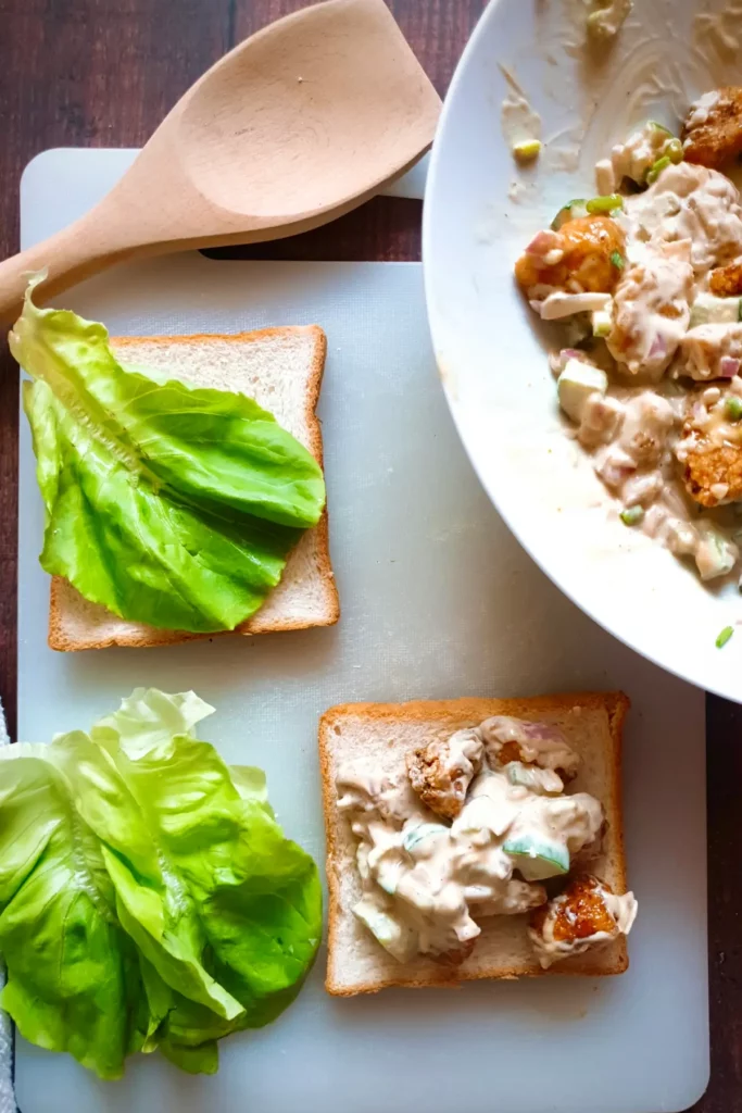 Gluten-free chicken salad recipe with fried chicken being poured on white sandwich bread along with lettuce.