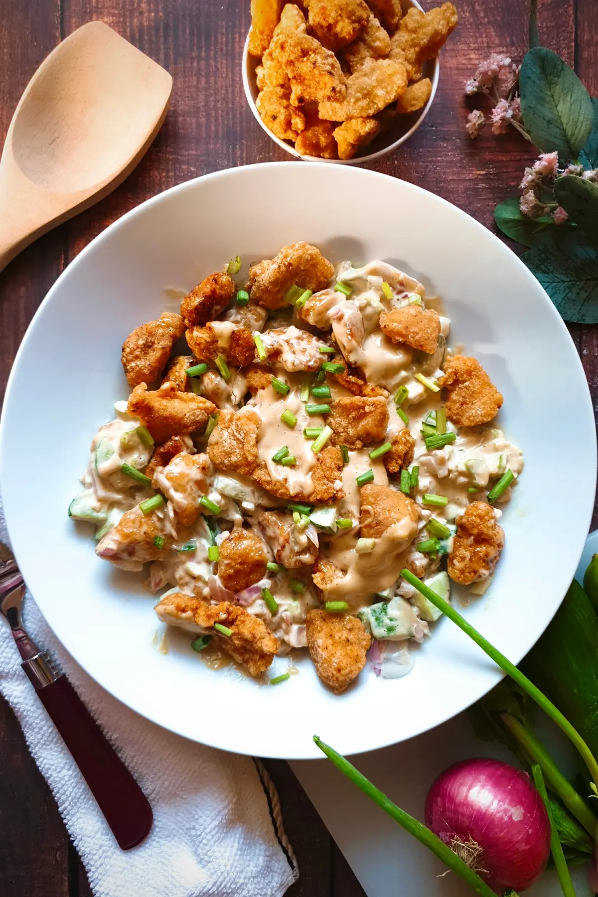 Easy Gluten-Free Chicken Salad Recipe with Fried Chicken on a white plate with a bowl of extra fried chicken pieces on top and raw ingredients like onion and green onion at the bottom.