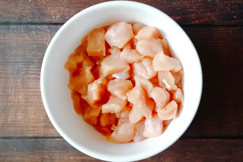 Small raw pieces of chicken in a white bowl.