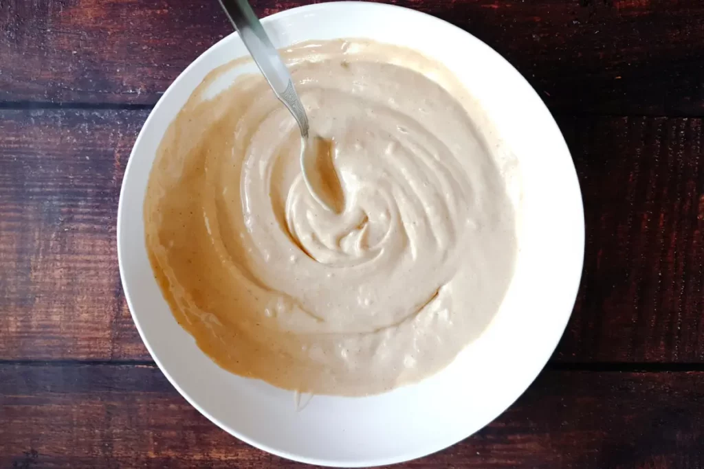 Salad dressing in a white mixing bowl being stirred completely with a spoon.